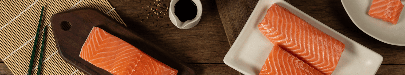Imagem do salmão fresco em cubos e lombo, servidos em pratos em cima de um fundo de madeira.